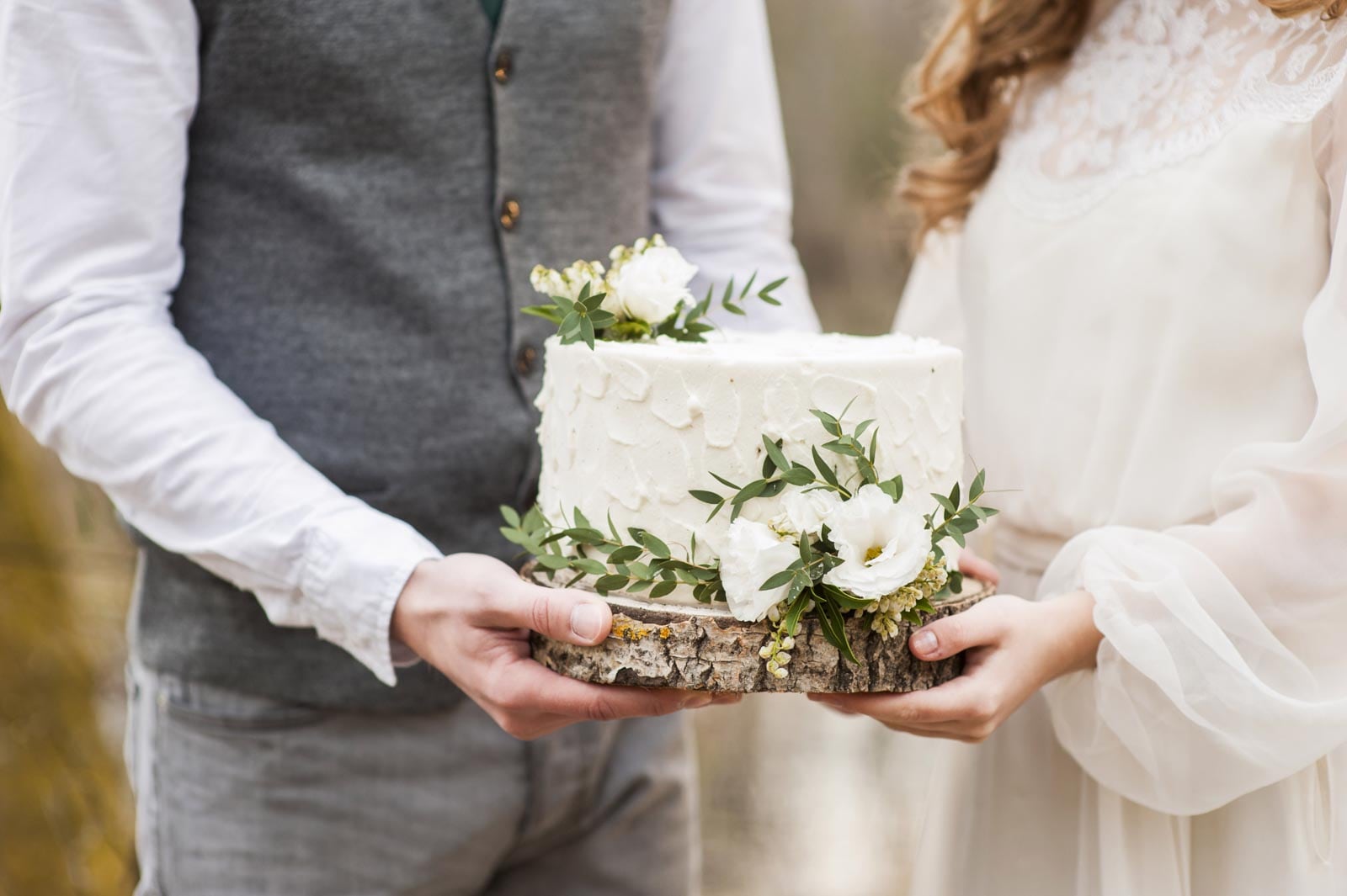 A bride and groom holding a wedding cake in the woods.