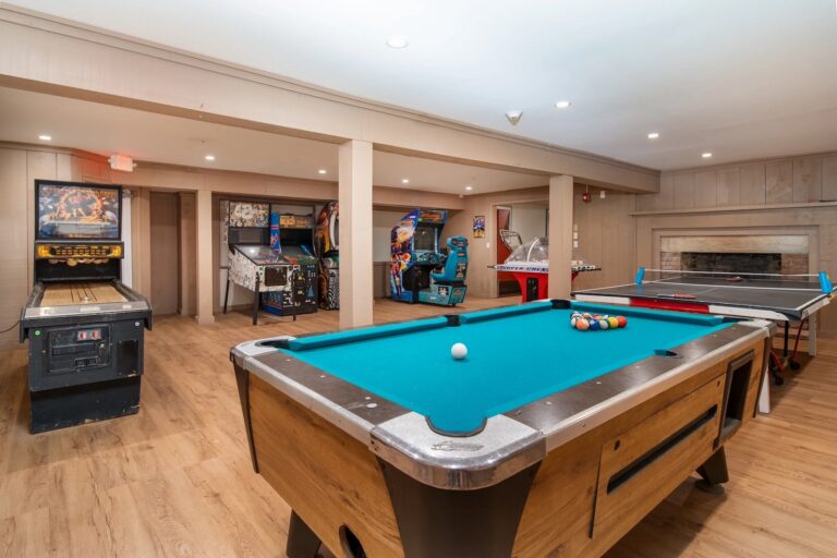 Game room with a pool table, air hockey table, pinball machines, arcade games, and a fireplace on wood flooring.